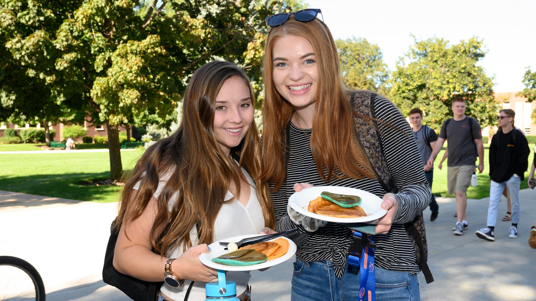 Two Boise State students smiling for a photo holding pancakes from the Alumni Association in the Quad