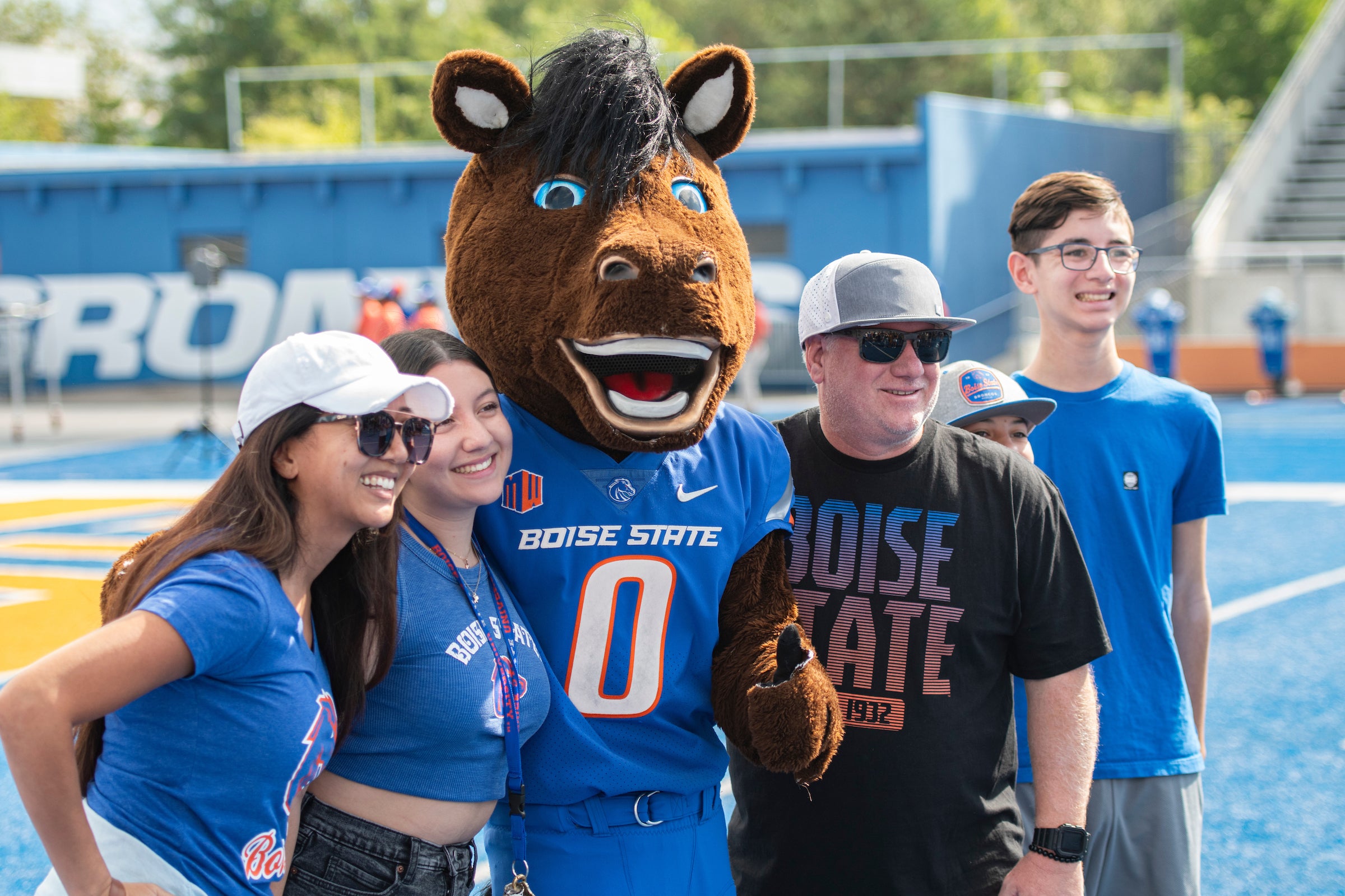 A Boise State family taking a photo with Buster Bronco on the Blue Turf