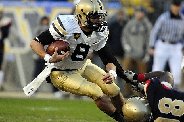 A football player carrying a football about to be tackled. 