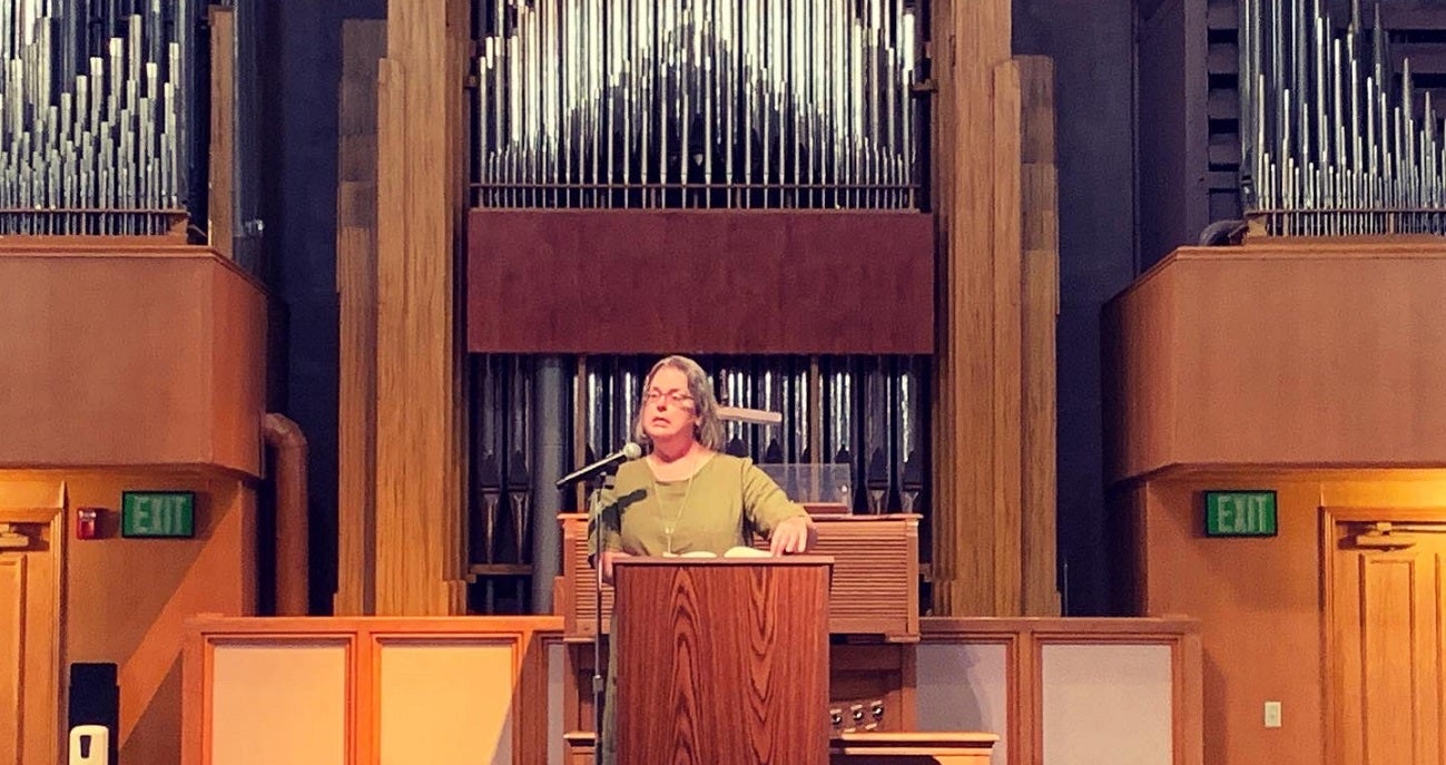 Kerri Webster reads at a podium in front of an organ