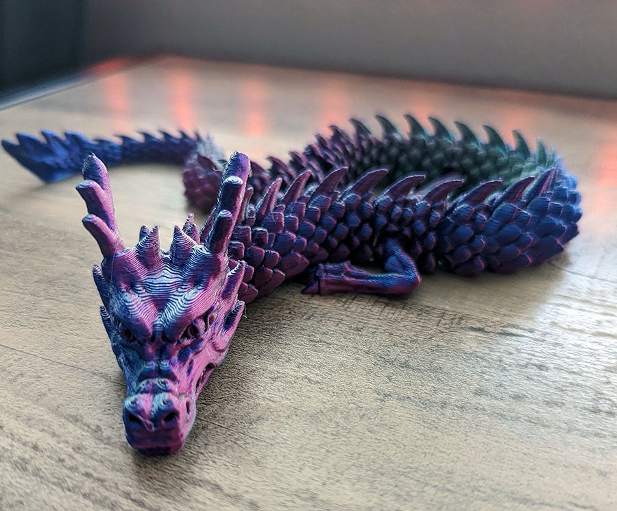A 3D printed plastic dragon prize resting on a light wooden surface