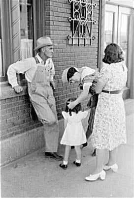 Man leans against building, woman is speaking to child, another woman looks on