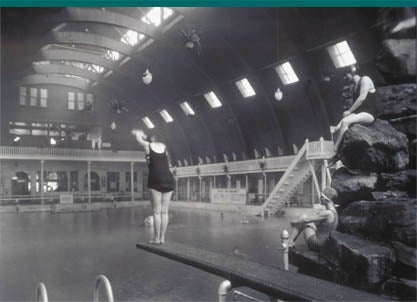 Swimmer enjoys a dive into the Natatorium's grand pool. Bathing beauties perch on natural rock.
