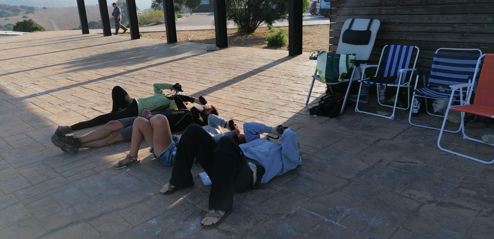 three scientists lay flat on their backs with binoculars pointed into the sky overhead
