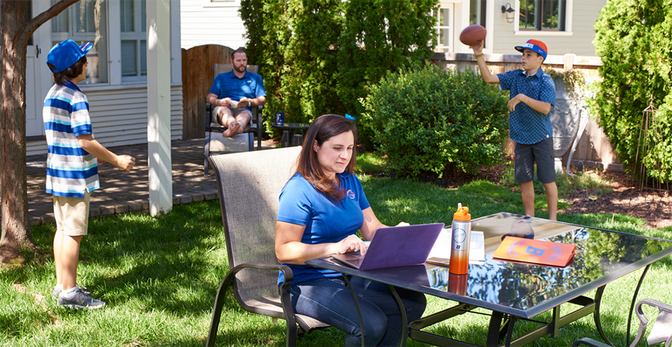 Online student in backyard studying with husband and 2 boys