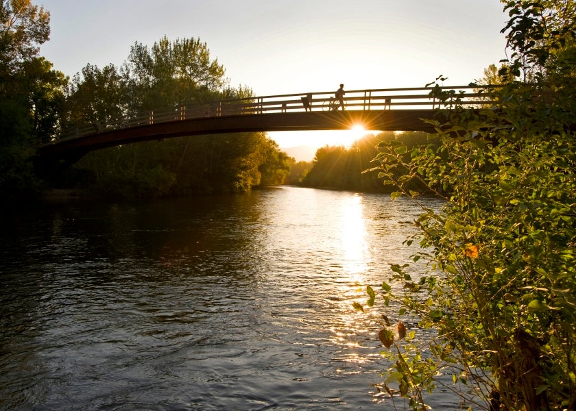 a person crossing Boise state friendship bridge with river and a setting sun
