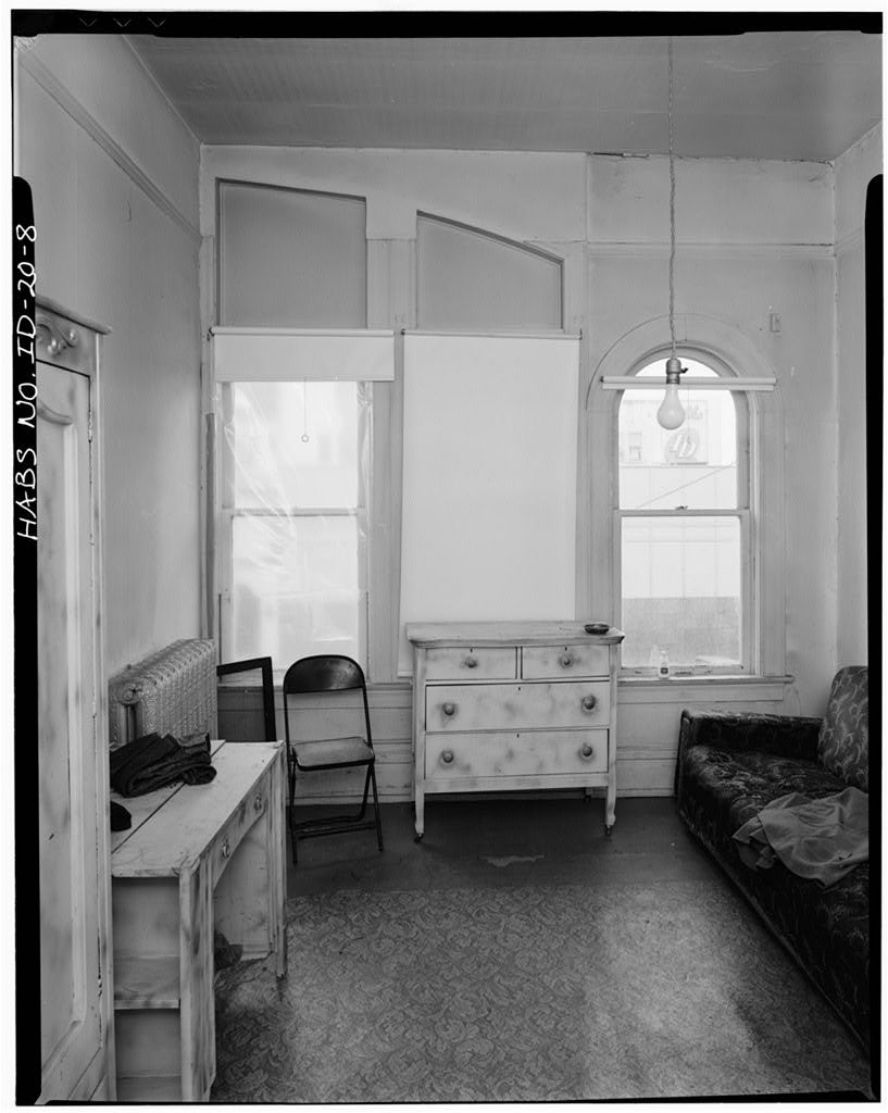 Black and white photo or room with a dresser, desk, and chairs