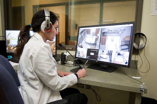 Nursing Faculty sits in control room watching simulated patient room