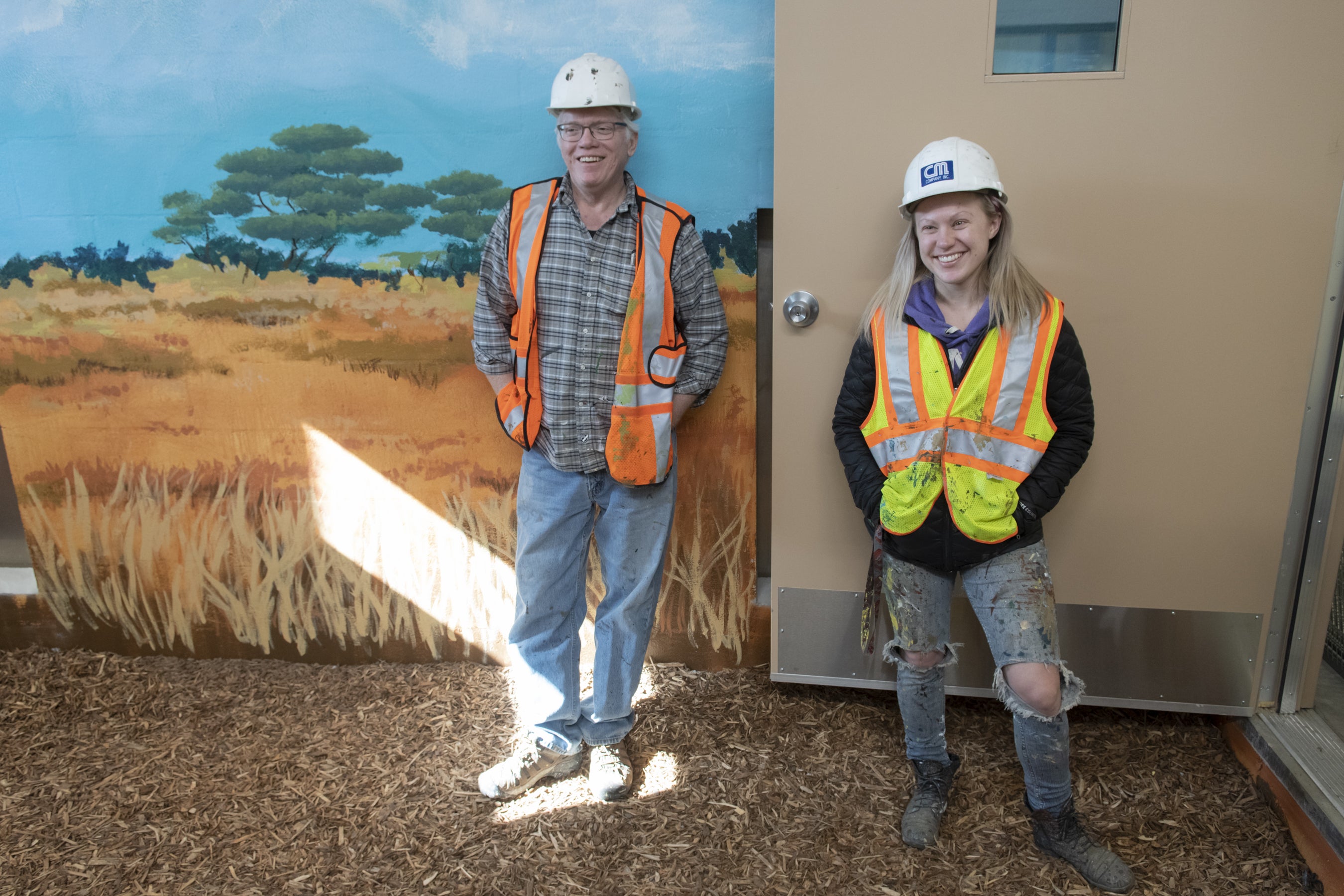 Two painters stand in front of a zoo mural.