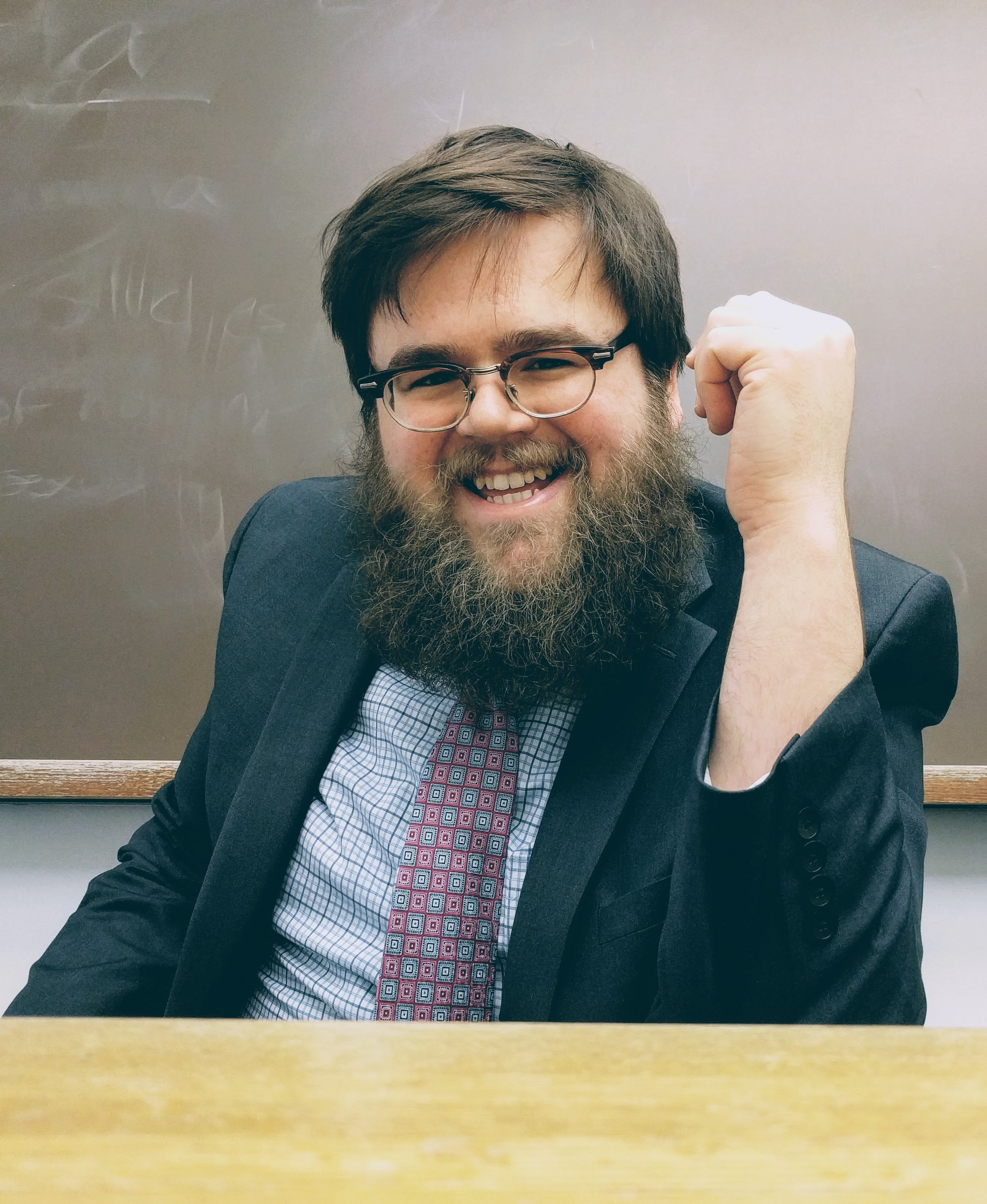 Guy with a beard smiling and fist pumping on a table.