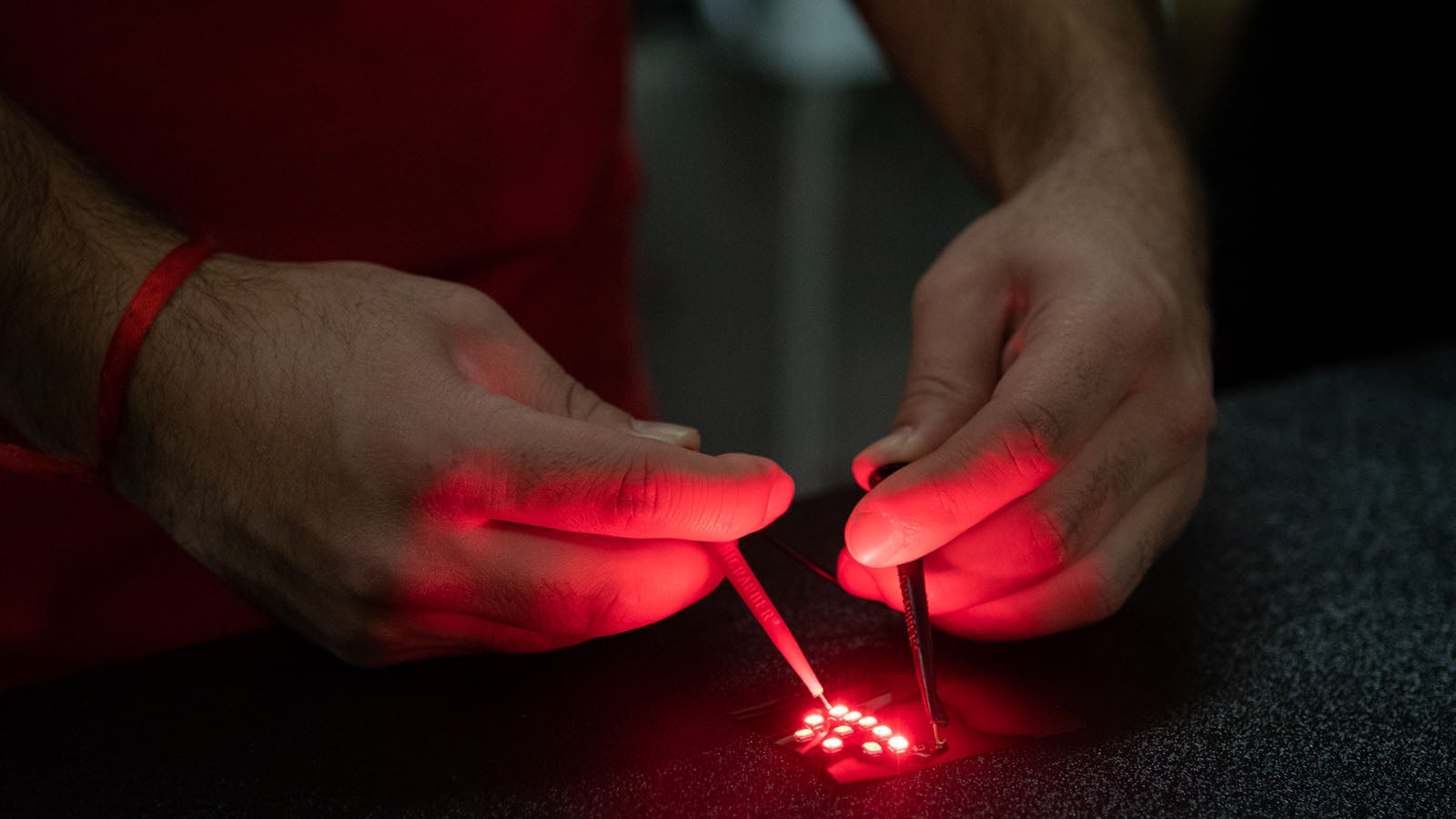 Two hands test the flexibile printed LED, emits red light