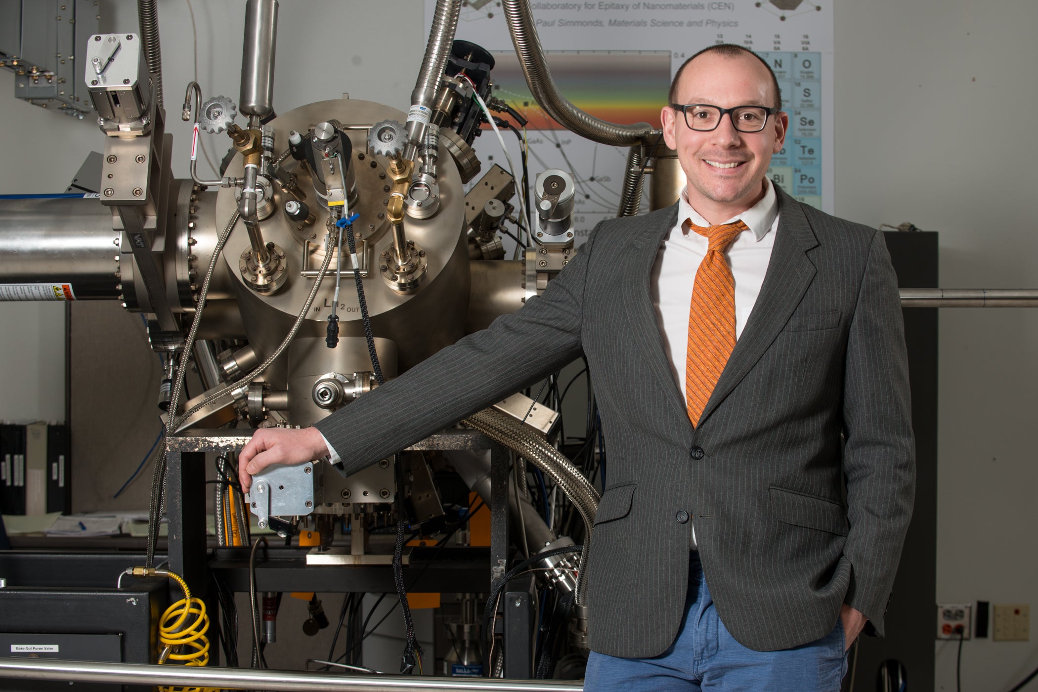 Photo of Simonds standing in front of Molecular Beam Epitaxy apparatus