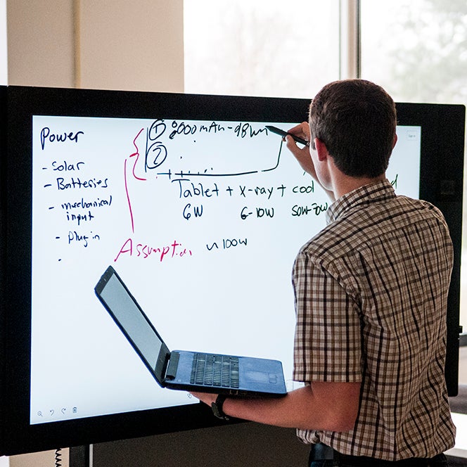 Students working on whiteboard while holding laptop