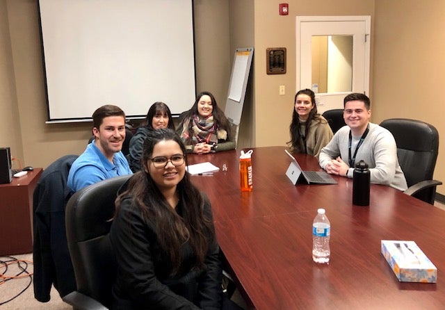Students smile around a conference table