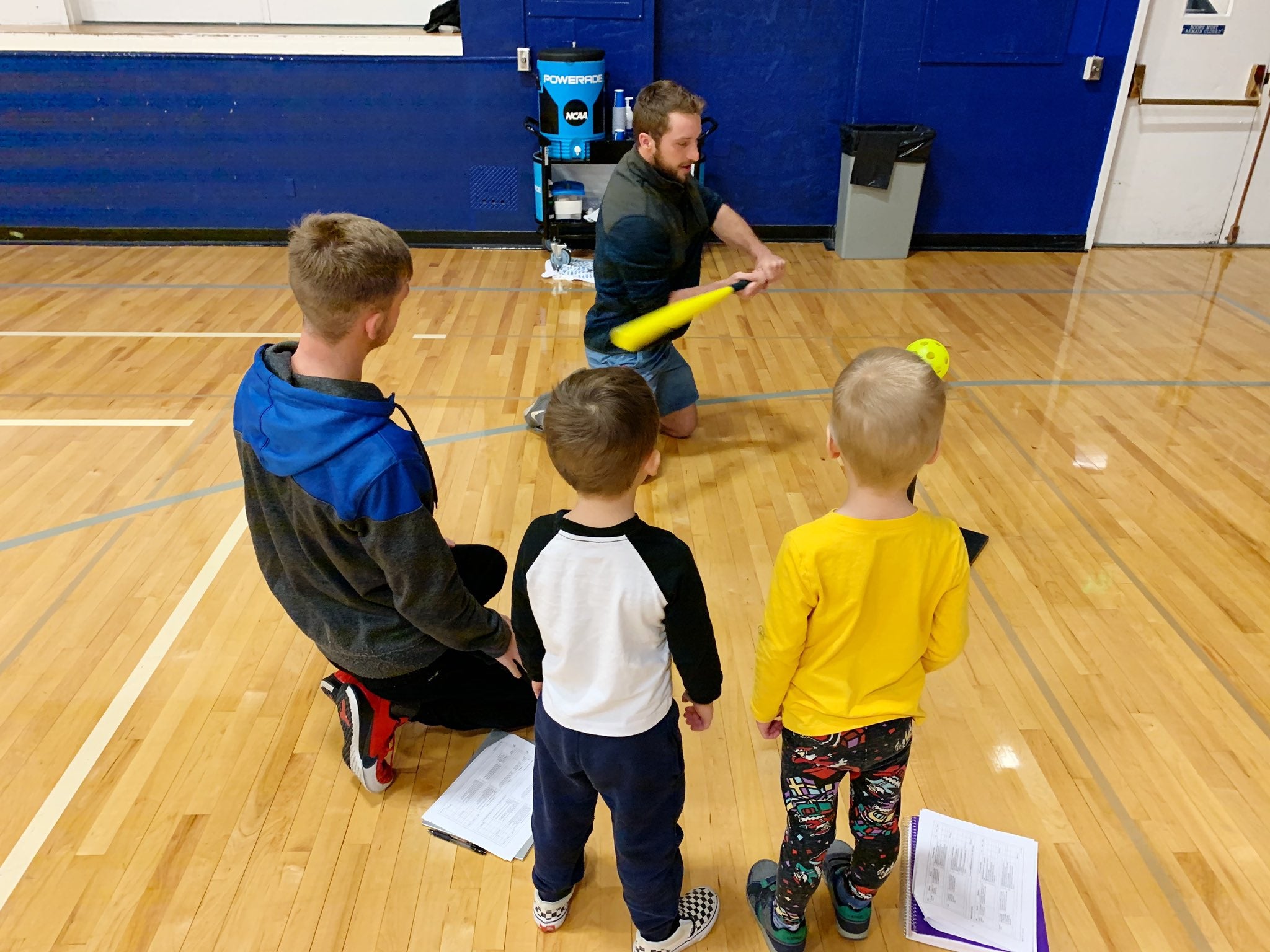 Kinesiology college student demonstrates batting techniques to preschoolers in BroncoGym