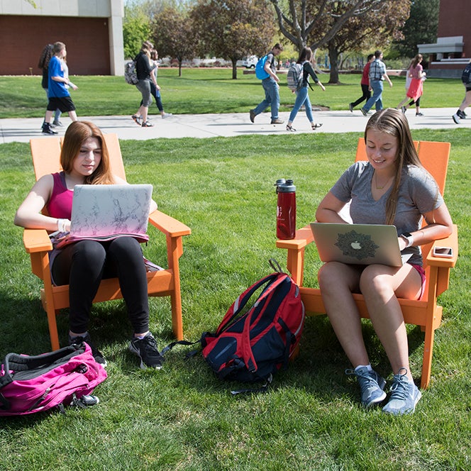 Freshmen Alma Ceja and Danielle Doerflein study on the quad between classes while on laptops and sitting in orange lounge chairs