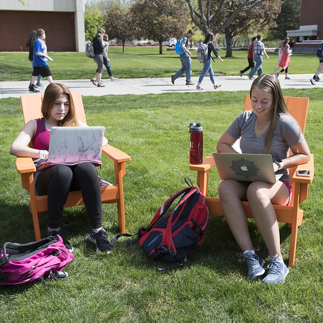 Students study on the quad while on laptops and sitting in orange lounge chairs