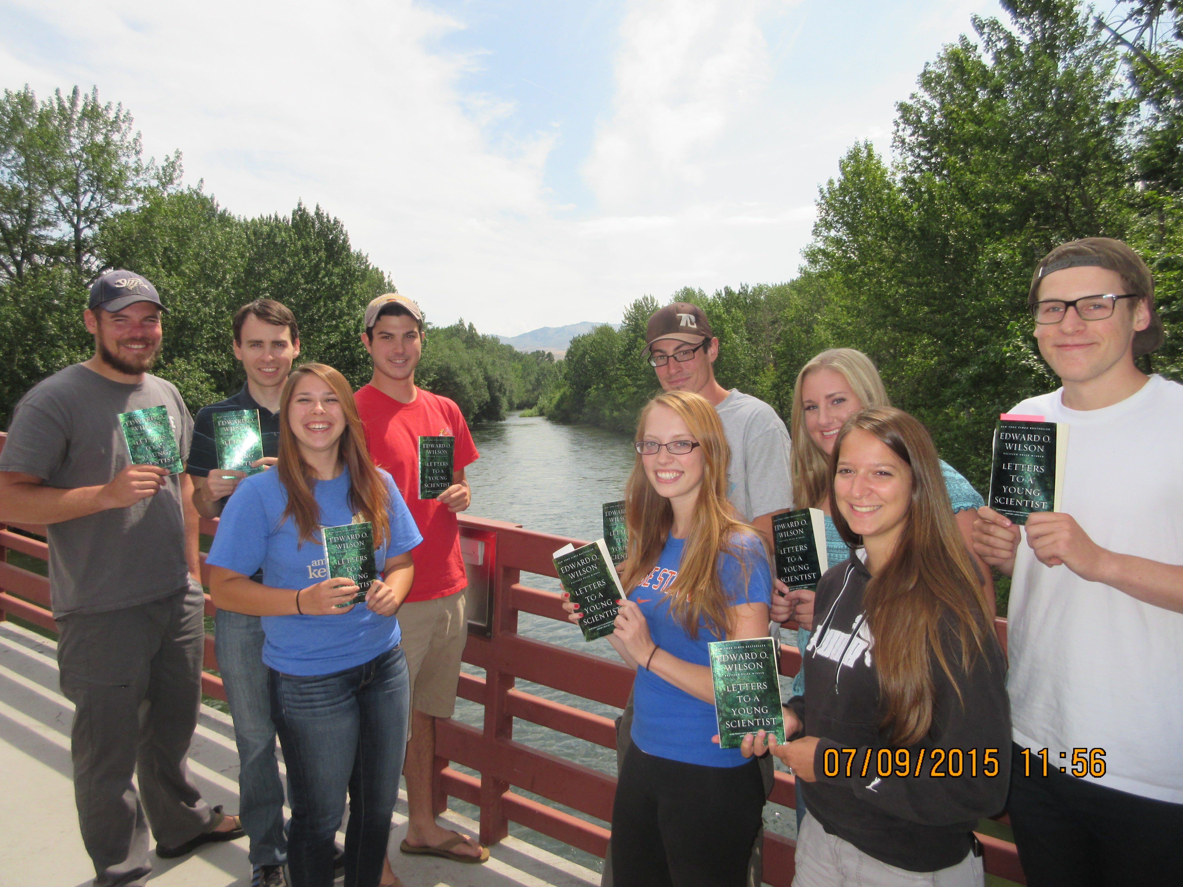 Students standing together on a bridge over the Boise River holding books