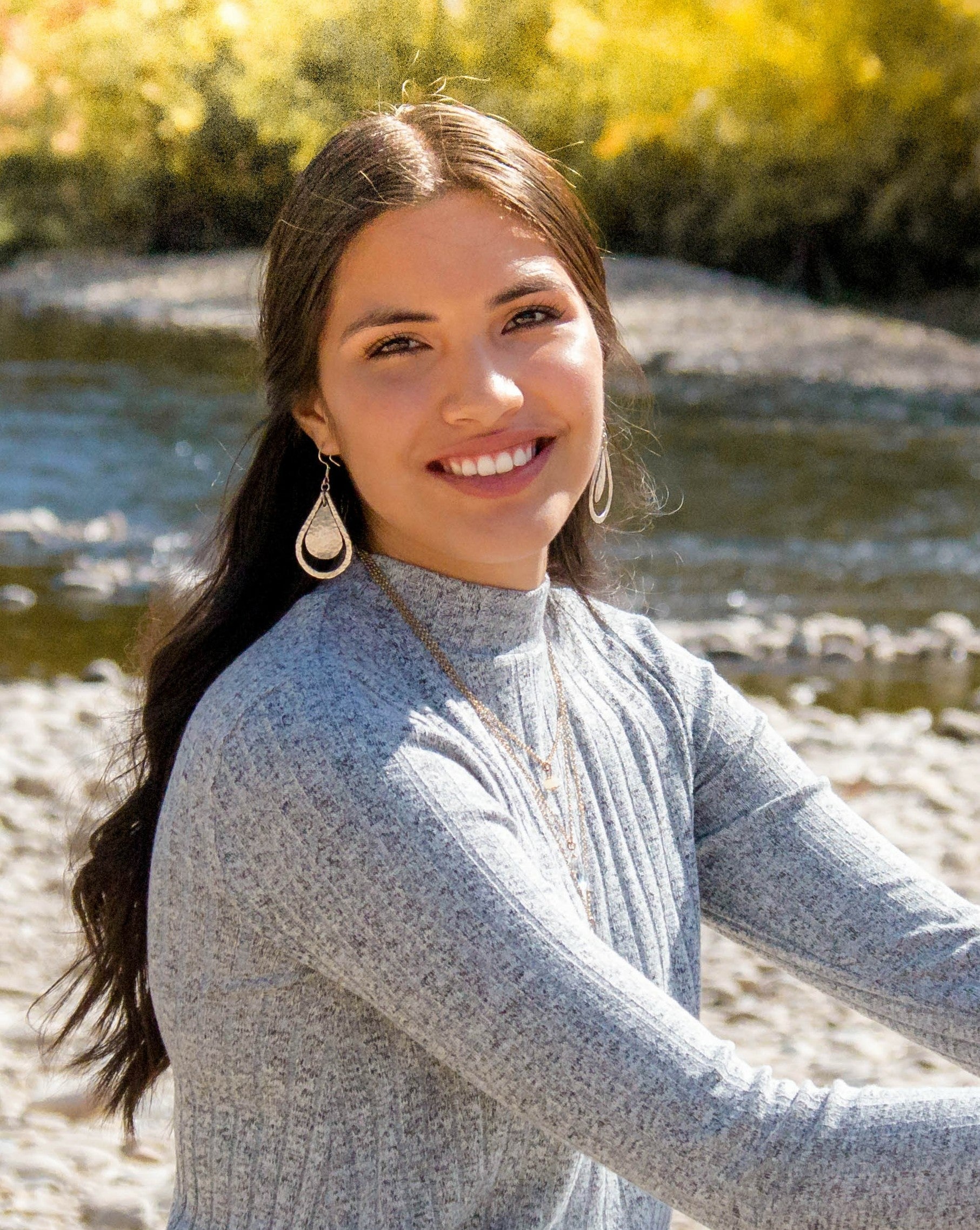 The author sits besides a river and smiles toward the camera.