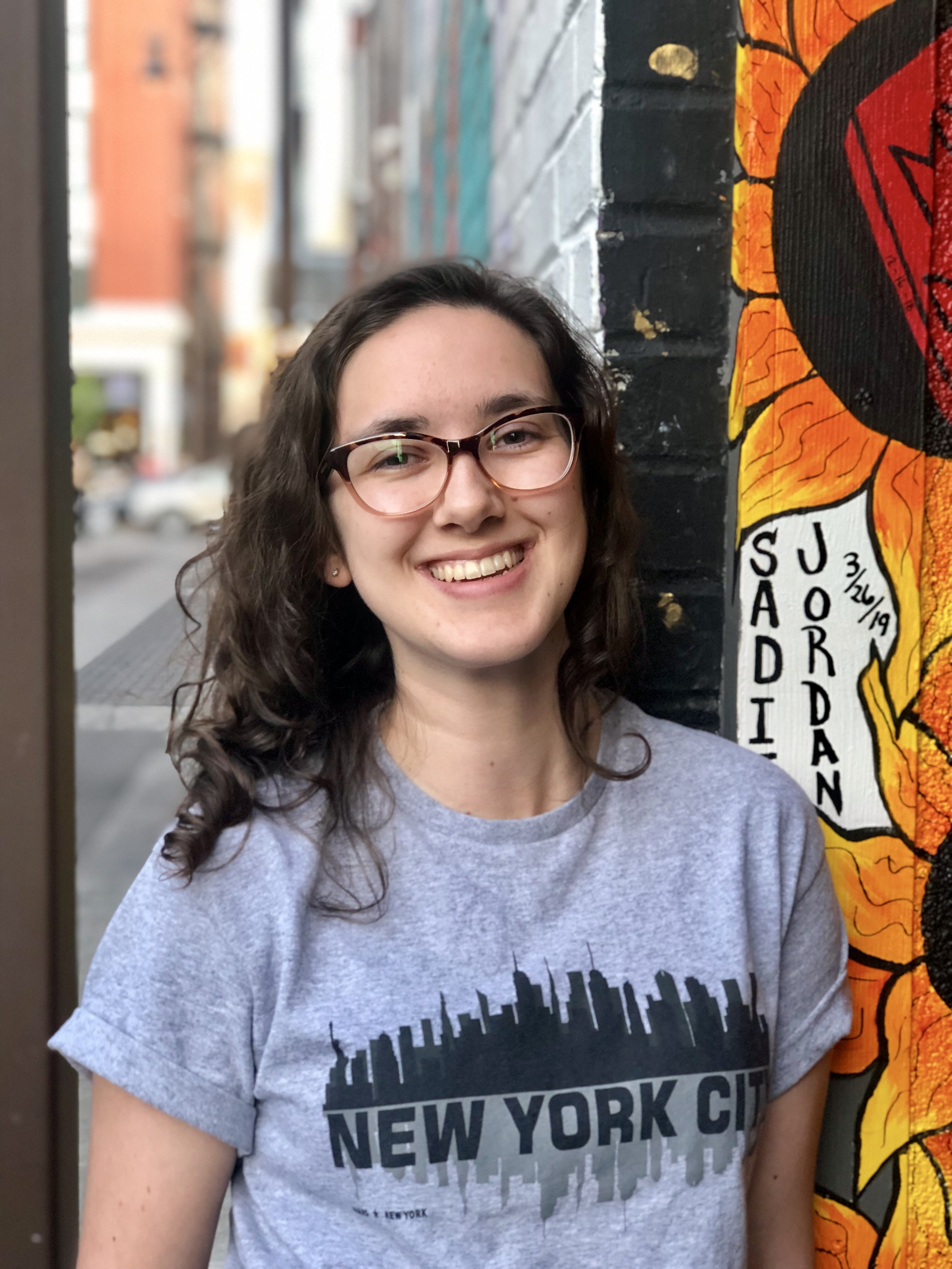 The author poses before a piece of street art and wears a New York City tee-shirt. 