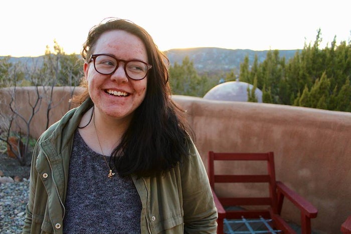 The author stands smiling in front of an adobe wall. 