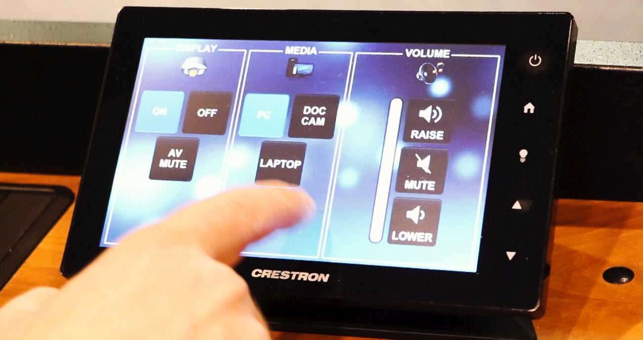 A hand taps the on button on the Crestron Control panel in a general classroom at Boise State