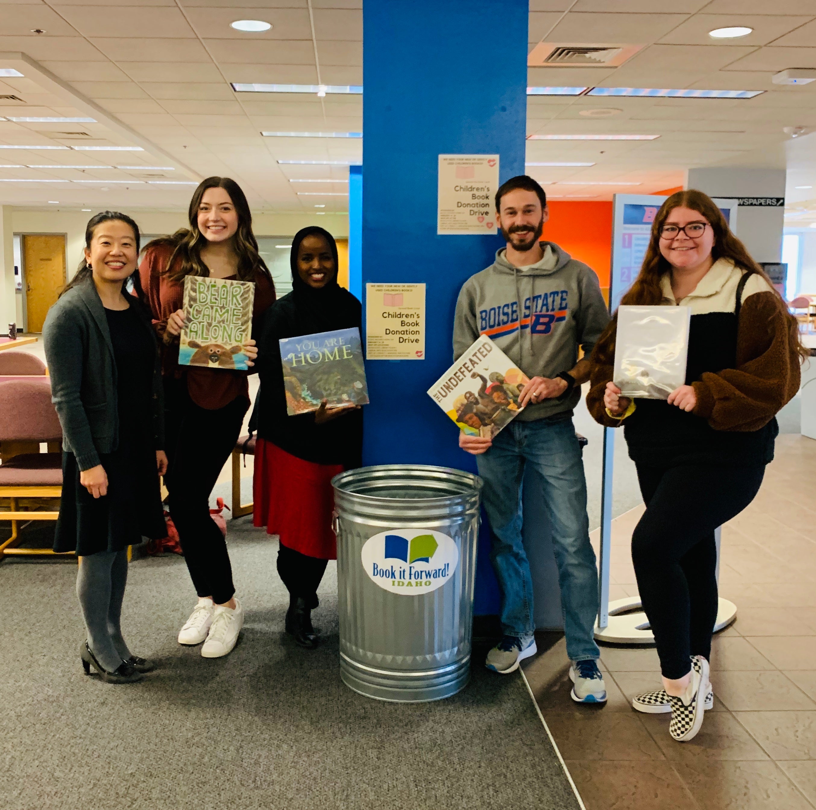 Students pose with books in front of Boot It Forward bin in Albertson's Library