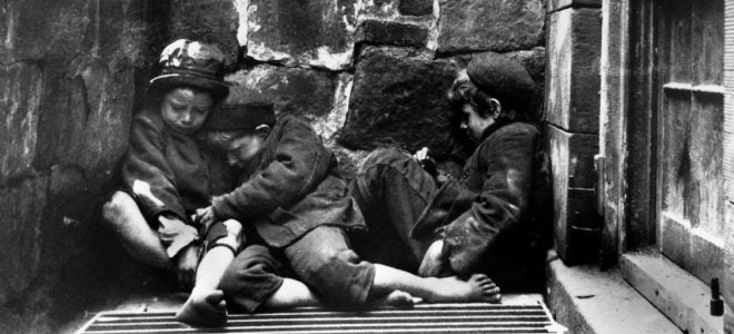 Three young children huddled together against a wall, black and white photo