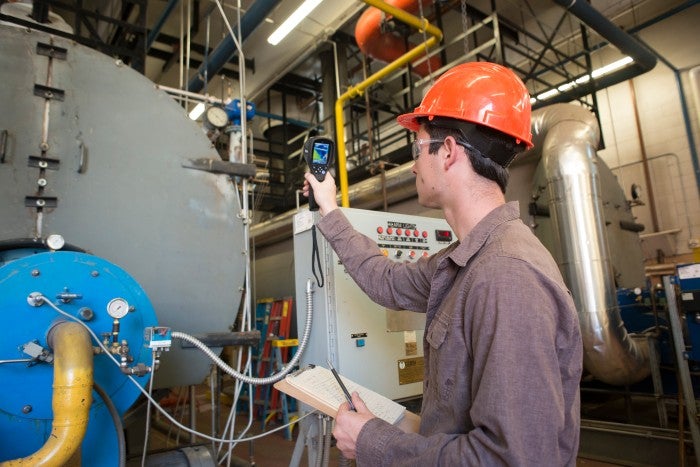 student in a hardhat taking readings in an industrial setting